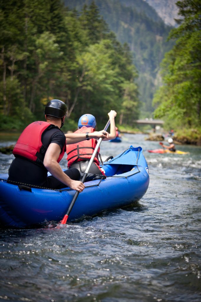People kayaking on a scenic river, surrounded by lush green trees and mountains.