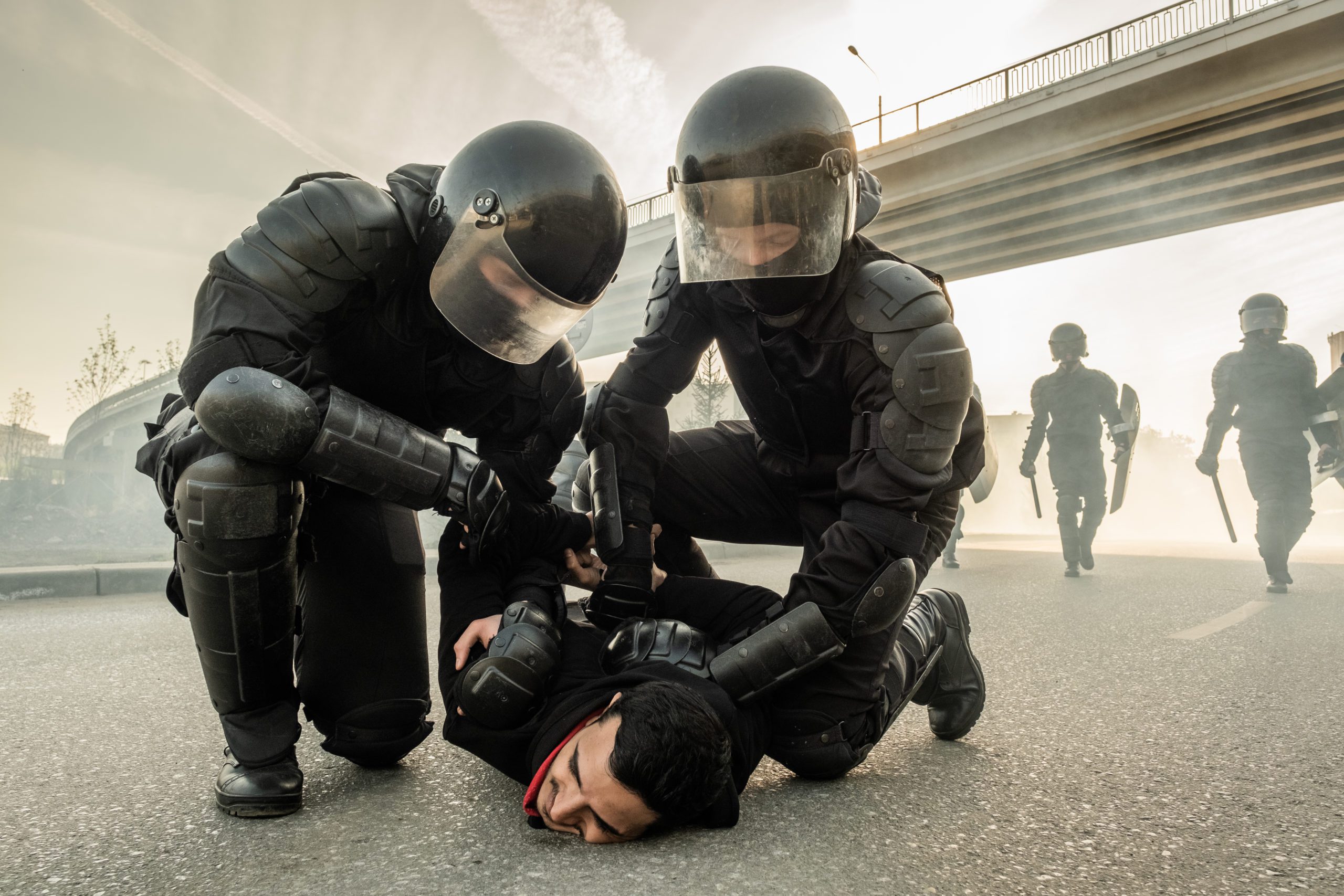 Riot police detain a protester on the ground during a demonstration under a highway bridge.