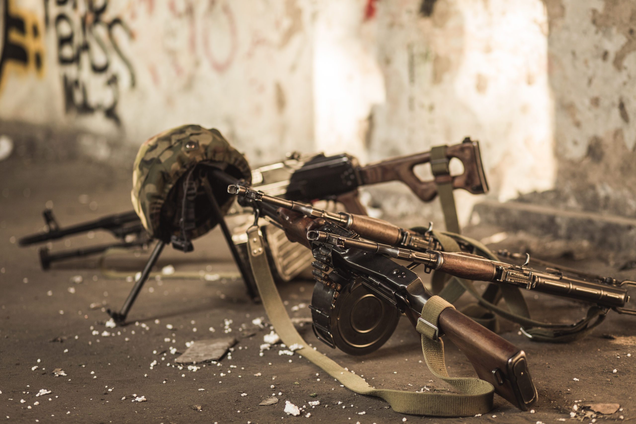 Military rifles and helmet on ground in abandoned building, suggesting warfare or conflict setting.