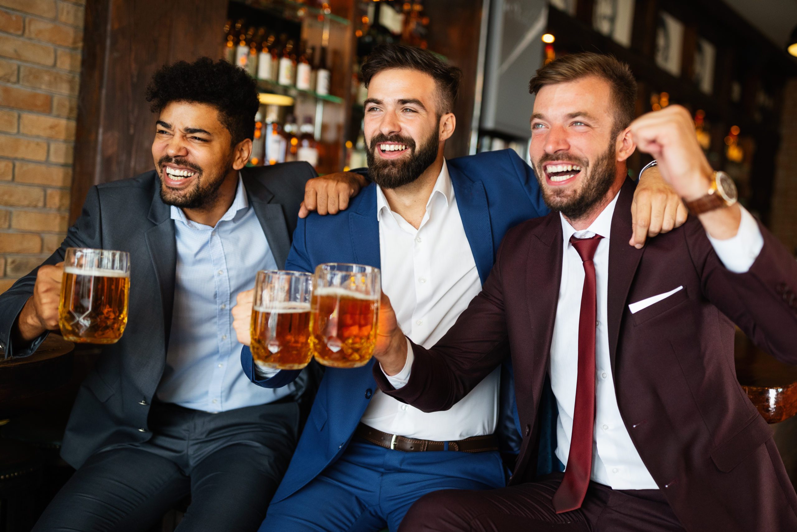 Three men in suits celebrating with beer in a bar, looking happy and cheerful.