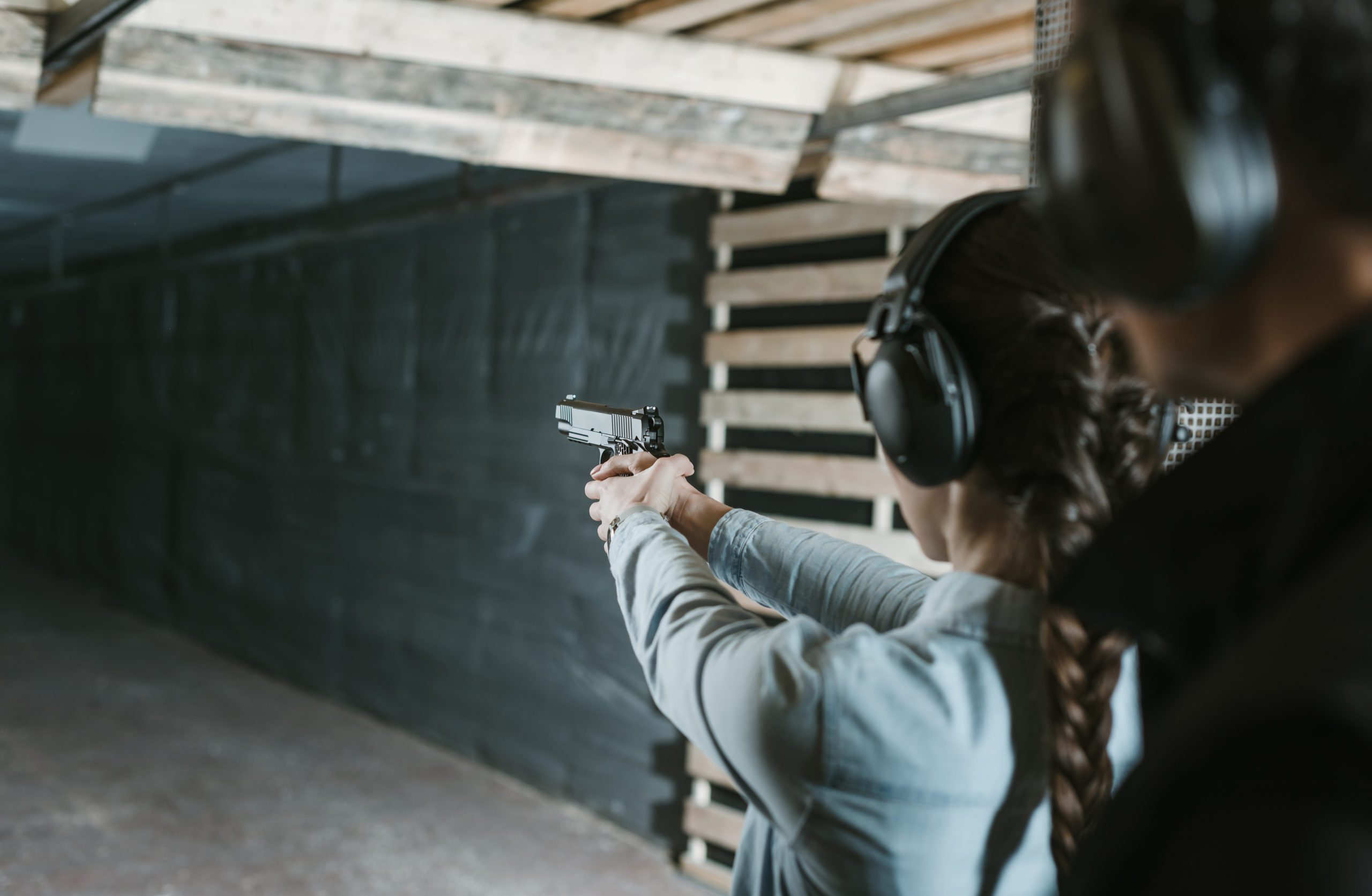 Person practicing shooting at indoor range wearing protective earmuffs and aiming handgun.