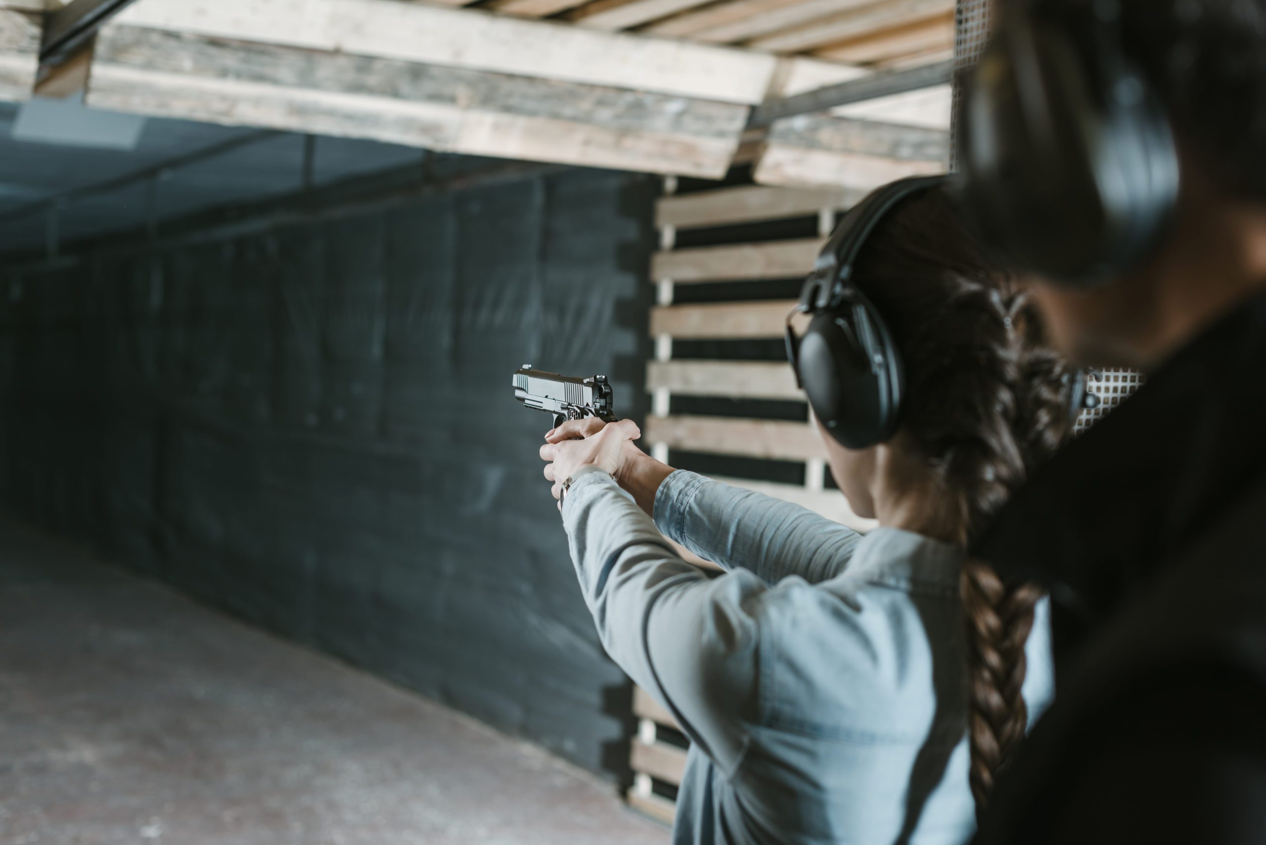 Person practicing shooting at indoor range wearing protective earmuffs and aiming handgun.