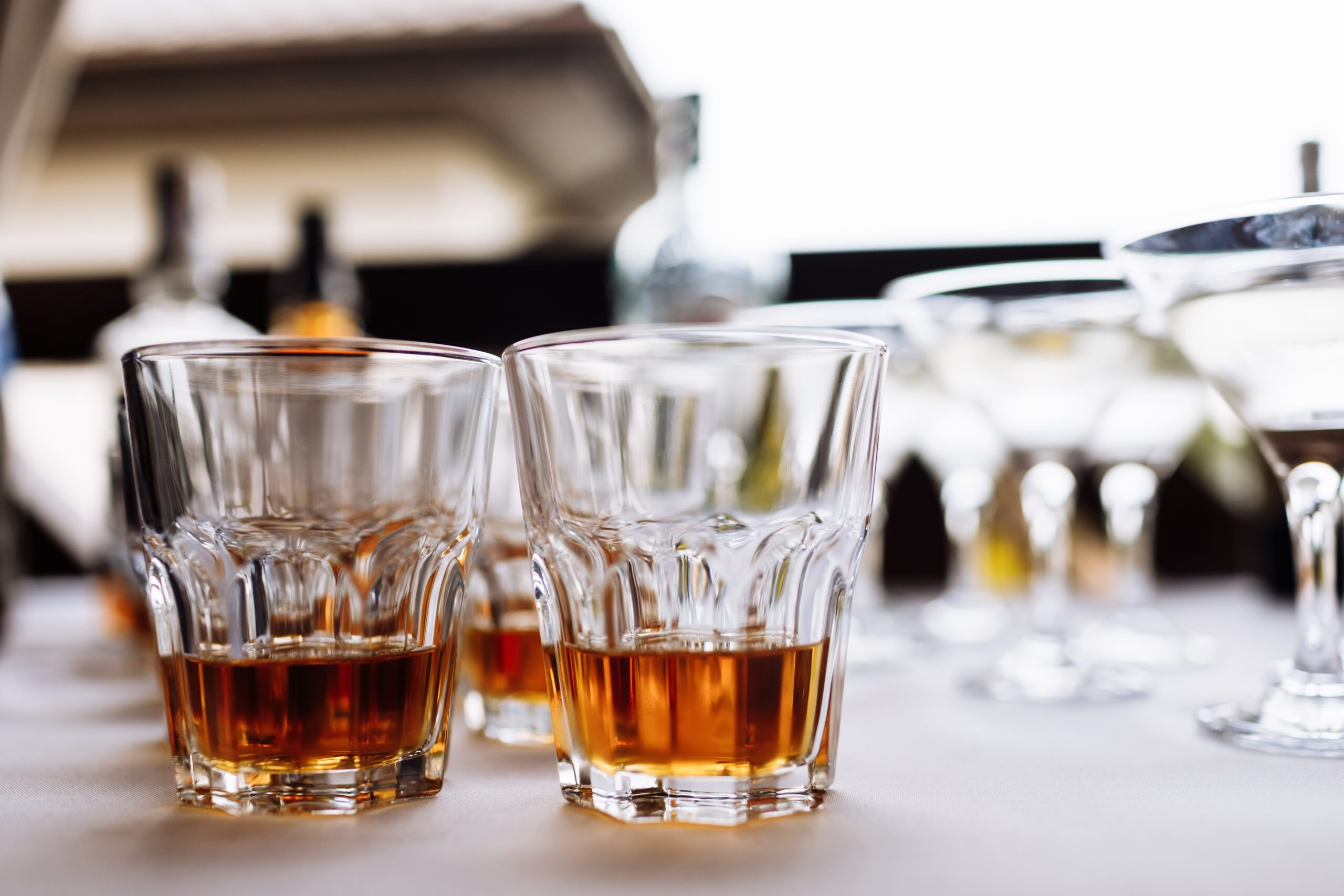 Two glasses of whiskey on a table with blurred bottles in the background, creating a classy bar atmosphere.