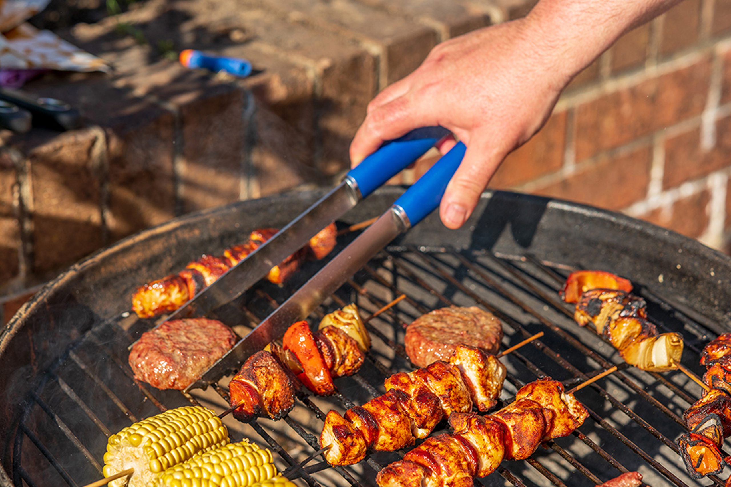Grilling skewers and burgers on a barbecue grill with corn on the cob, outdoor cooking scene.