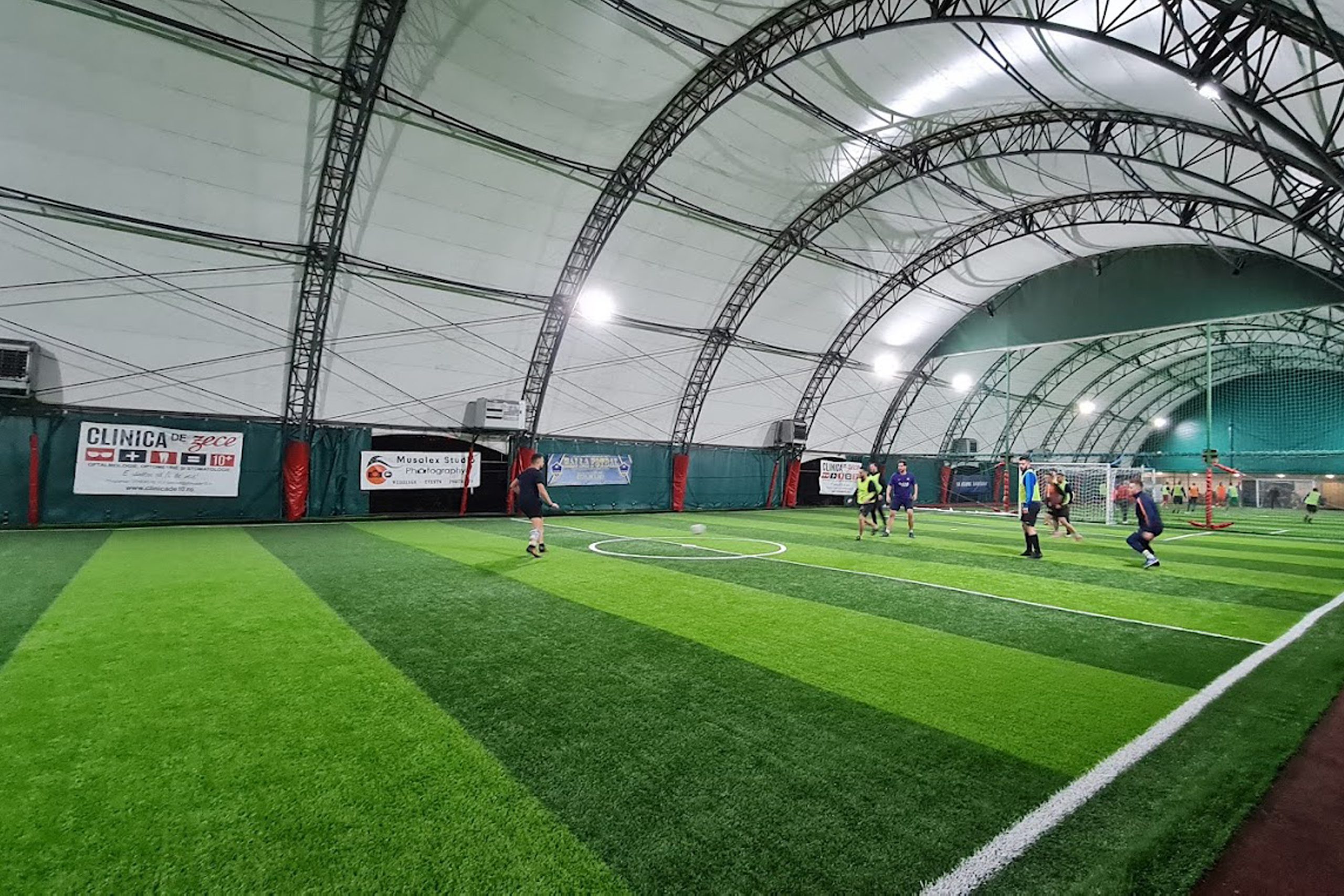 Indoor soccer game on artificial turf field under large lit dome, players in motion toward the goal.