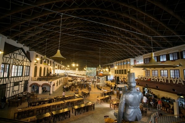 Spacious indoor beer hall with arched ceiling and wooden tables, featuring a central statue and traditional architecture.