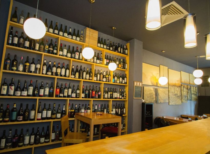 10256774_1095773843771563_2966362166853849874_o-big Cozy wine bar with a vast collection of bottles on shelves, ambient lighting, and a warm wooden interior.