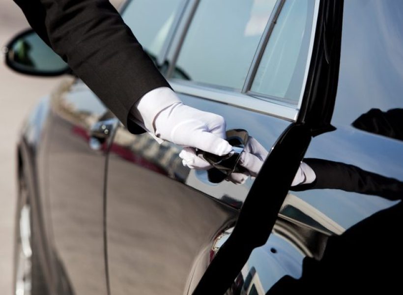 Chauffeur opening luxury car door with white gloves, providing premium transportation service.