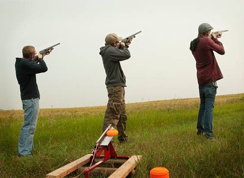 Three men  target practising with clay  pigeons, on a cloudy day