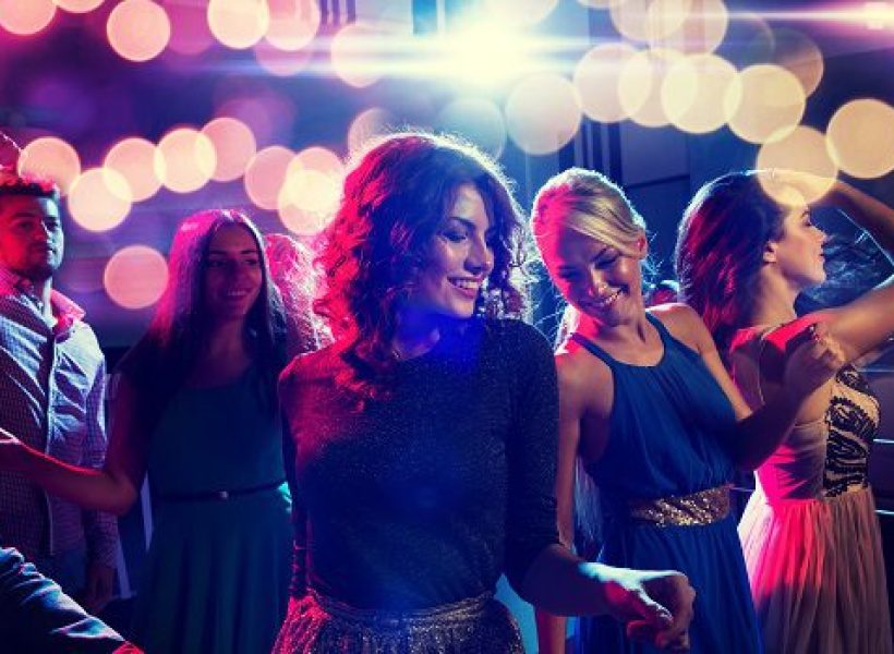 Young people dancing joyfully in a nightclub with colorful lights creating a vibrant party atmosphere.