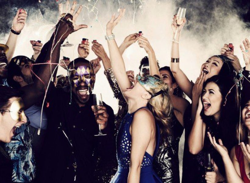 A lively masquerade party with joyful people celebrating, wearing masks and raising glasses amid confetti and smoke.