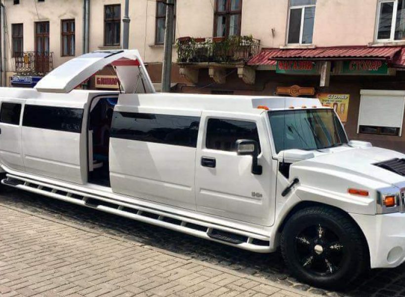 White stretch Hummer limousine parked on a cobblestone street in front of vintage buildings.