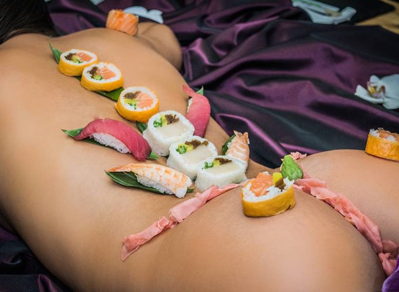 A creative sushi arrangement on a flat surface with a dark silk background, featuring various types of sushi.