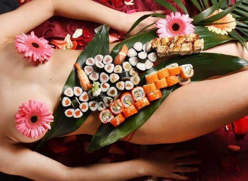 Aesthetic sushi platter with vibrant flowers arranged on a person adorned with tropical leaves.