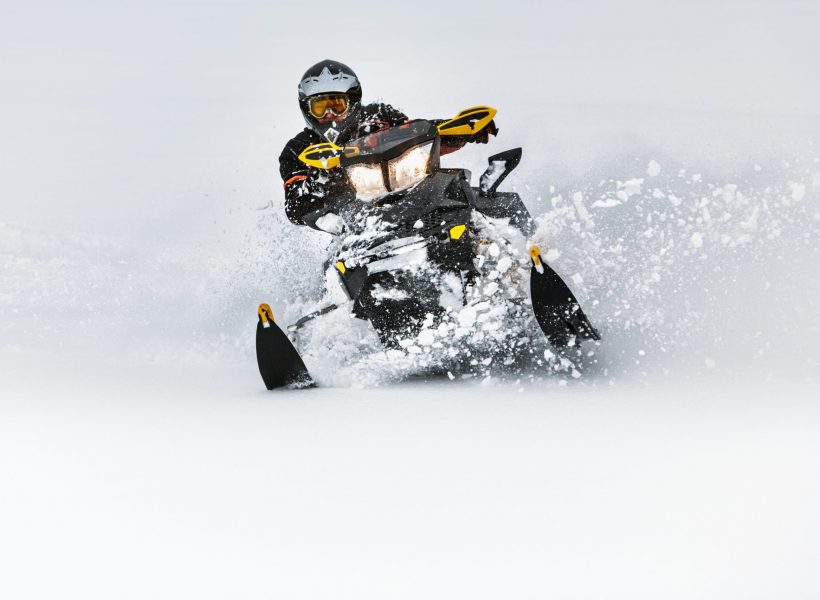 In deep snowdrift snowmobile rider make fast turn. Riding with fun in deep snow powder during backcountry tour. Extreme sport adventure, outdoor activity during winter holiday on ski mountain resort.