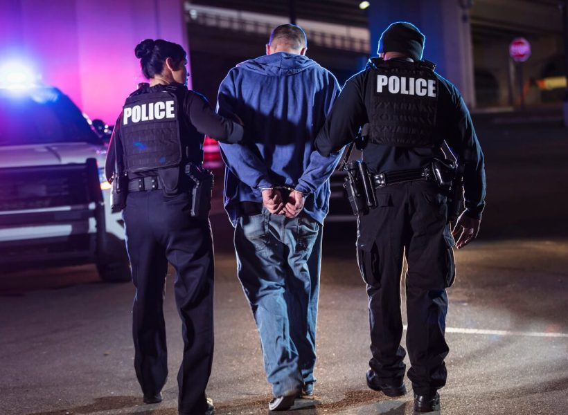 ask-the-attorney-what-is-the-difference-between-being-under-arrest-and-detained-for-questioning Police arresting a handcuffed individual at night, patrol car lights flashing in background.