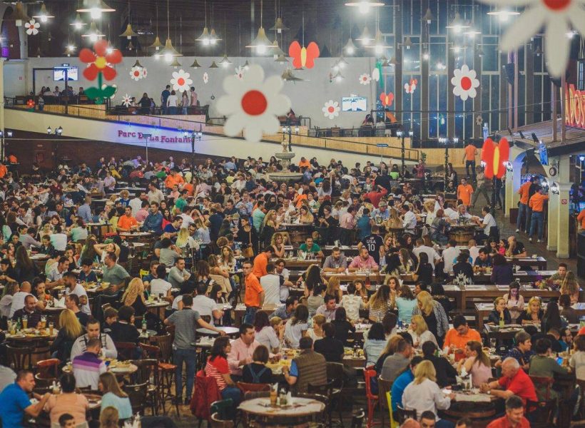 Crowded restaurant with people enjoying meals and drinks under festive floral decorations.
