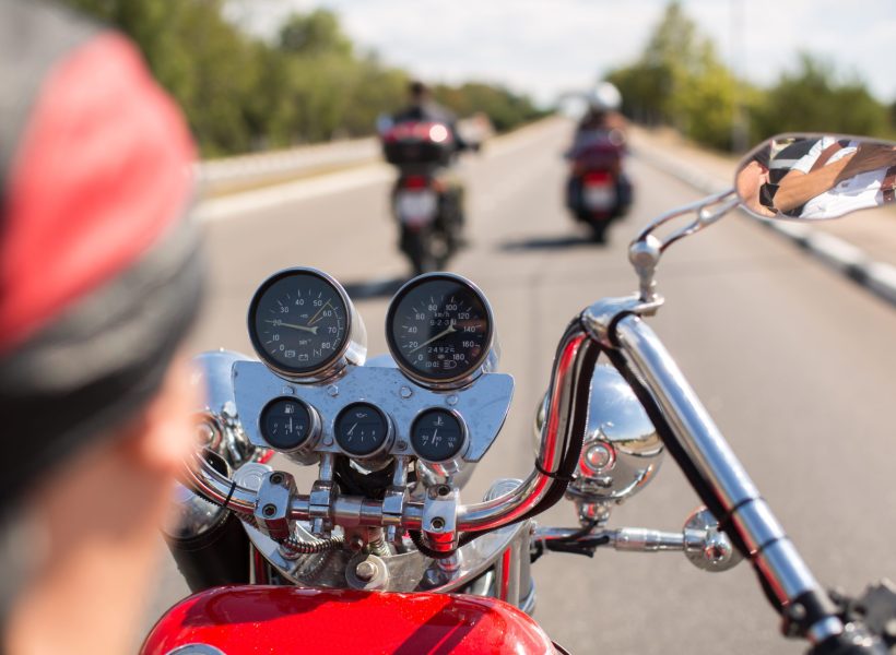 Biker riding motorcycle on road in morning sunny day. Shot from behind