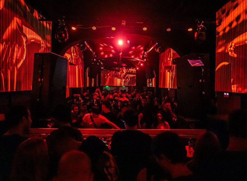 Crowded nightclub with vibrant red lighting and lively atmosphere.