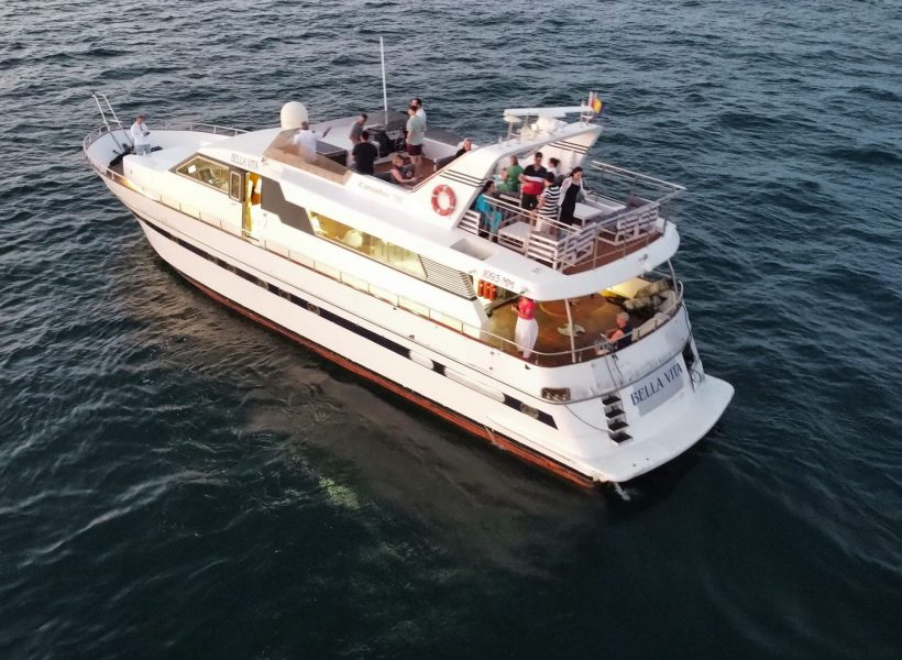 dji_fly_20230715_210502_634_1689444319846_photo_optimized-scaled Luxury yacht on the ocean at sunset with people on deck enjoying the view.