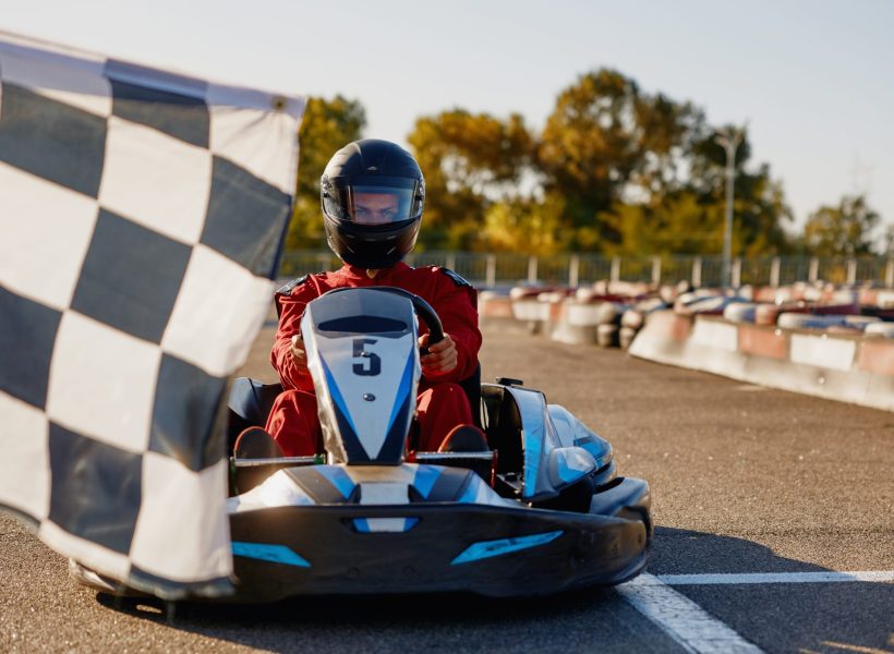 Go-kart driver crossing at finish line moving to checkered racing flag. Active battle win for first place in extreme auto sports championship