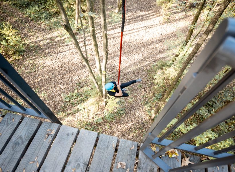 Man jumping from a bungee tower, having an active recreation in a rope park in the forest