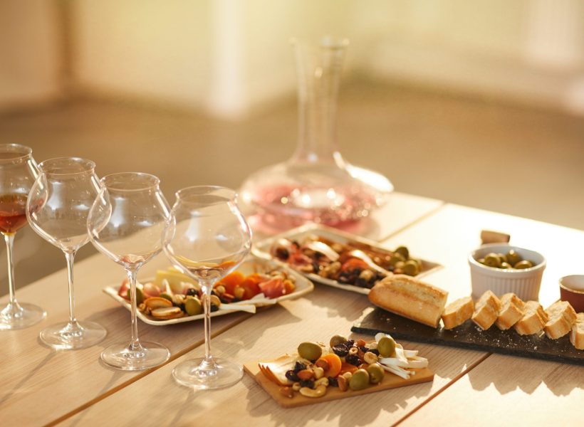 Background image of wine glasses on wooden table with rustic snacks set for wine tasting session in sunlight, copy space